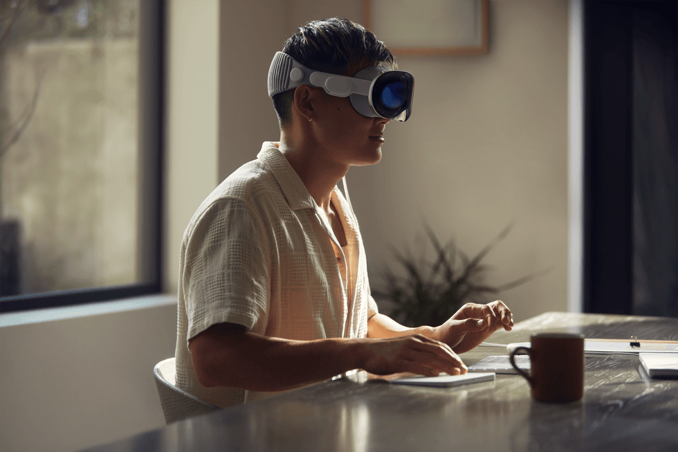 a man sits at a desk typing on a keyboard with a mouse using the vision pro