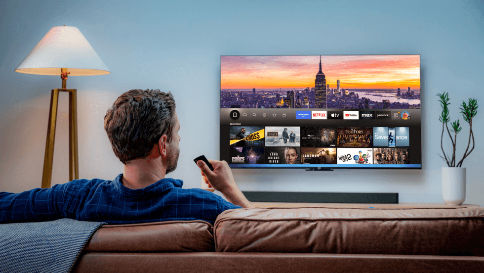 a man sits on a sofa and uses the alexa voice control to control whats' on-screen