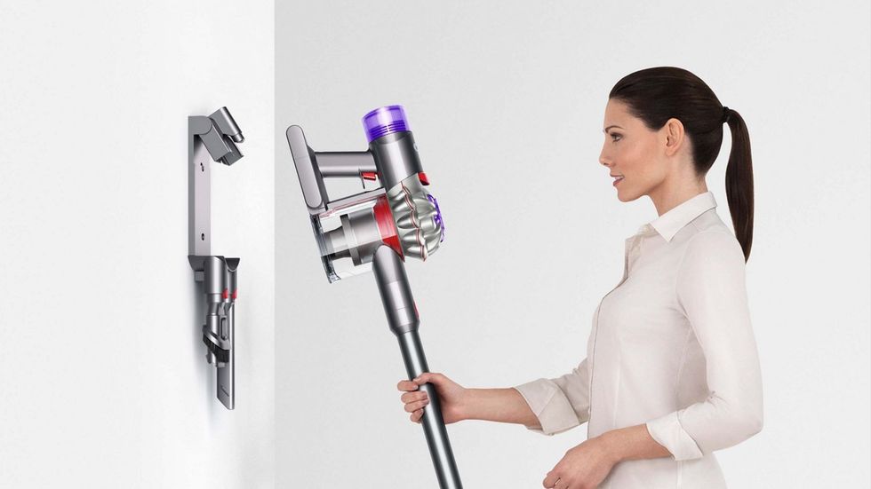 a woman puts the dyson v8 cordless vacuum into the charging dock mounted on a wall