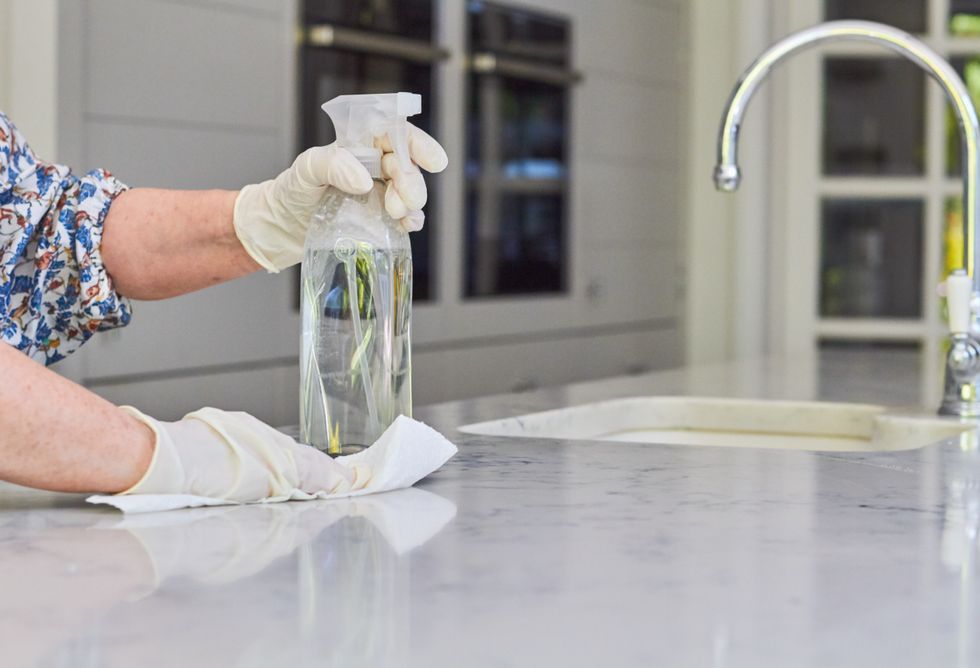 A woman wearing rubber gloves to clean a kitchen counter, holding a spray bottle