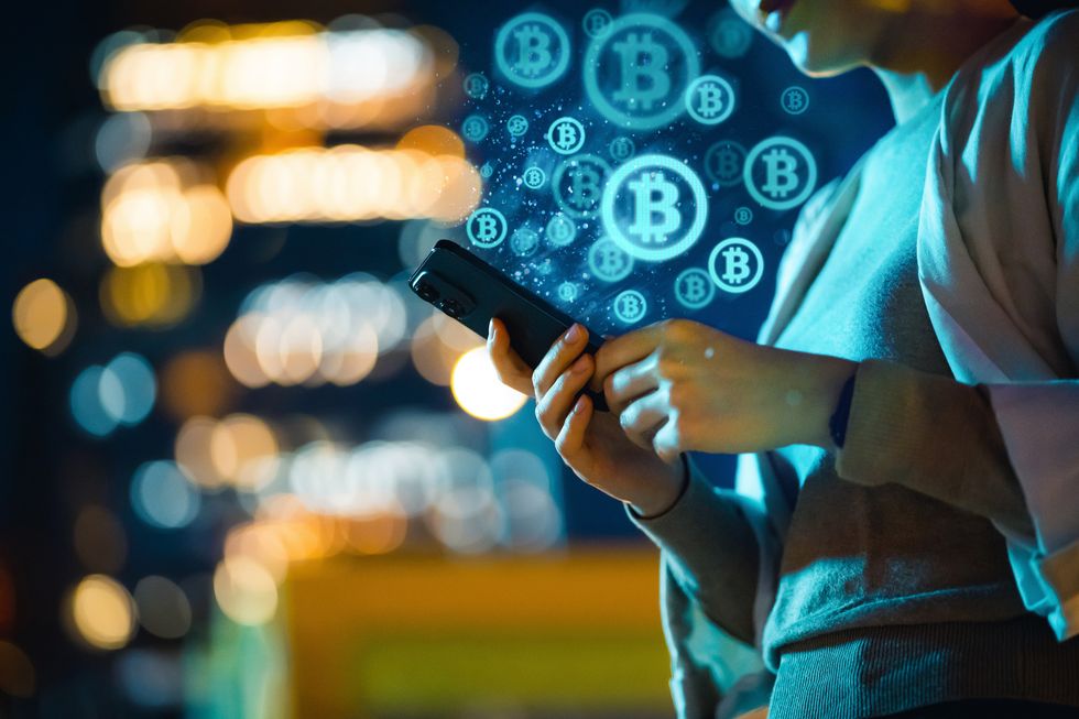 Bitcoin logo in background and person checks phone