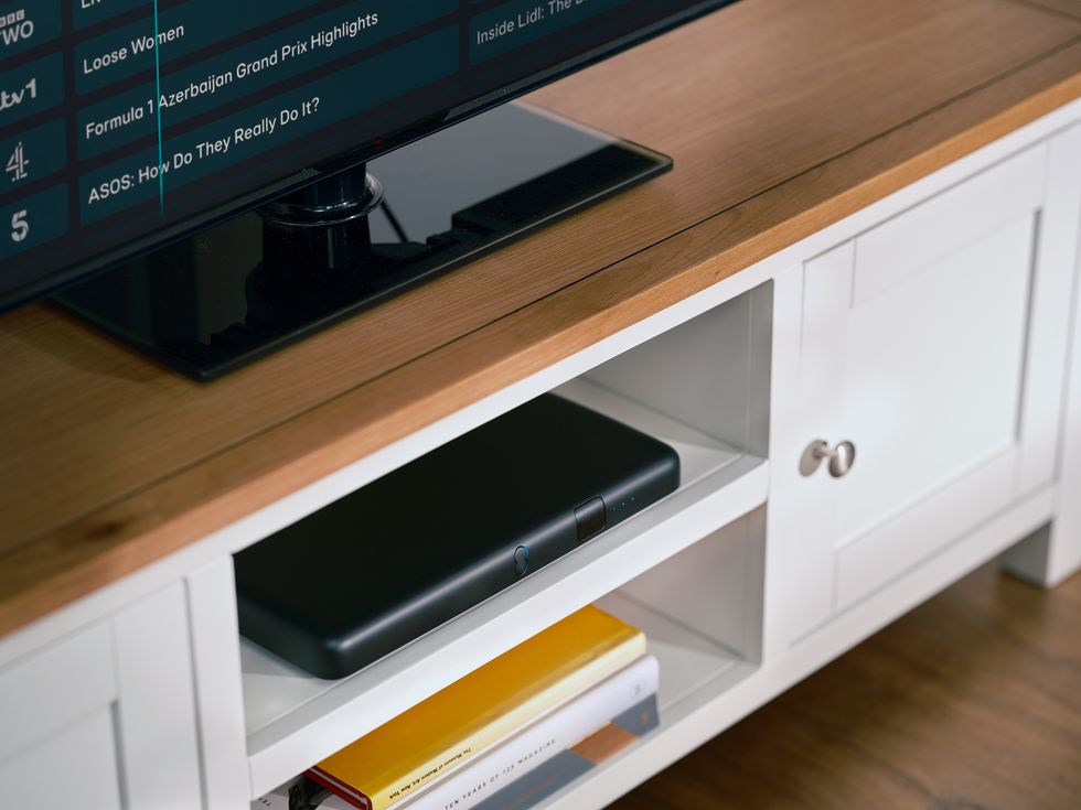 ee tv box pro pictured in a media unit with a flatscreen tv showing the latest live listings above