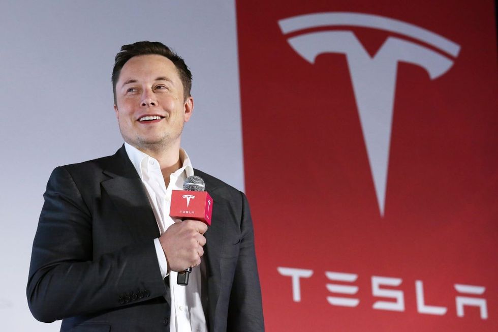 Elon Musk stood next to a Tesla sign