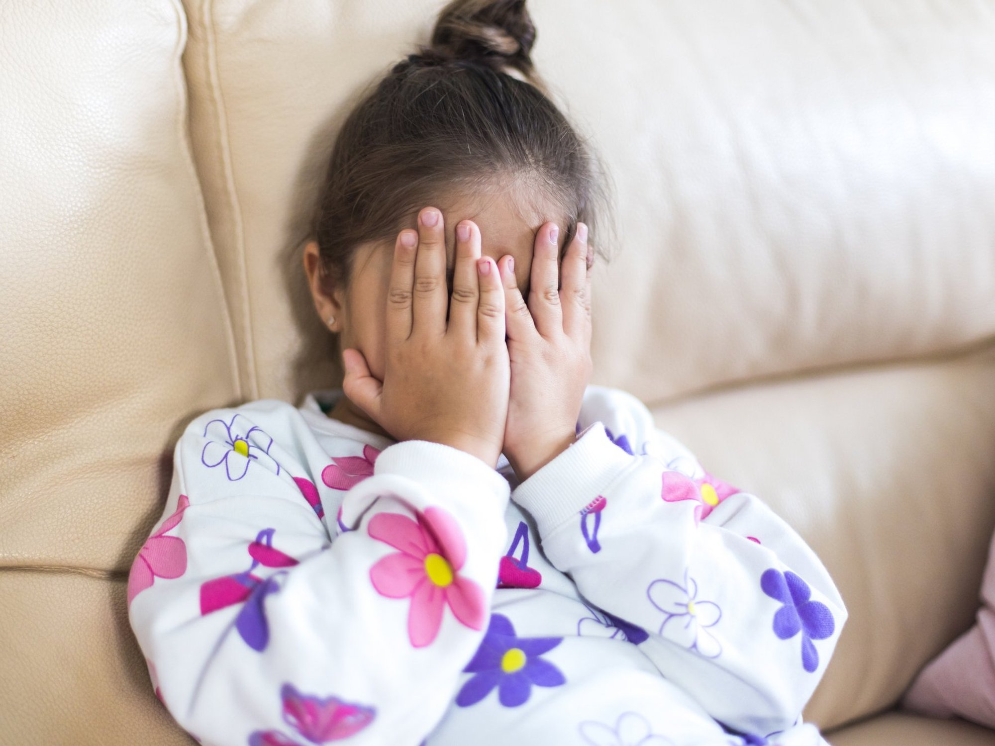 Girl sits on sofa covering face with eyes
