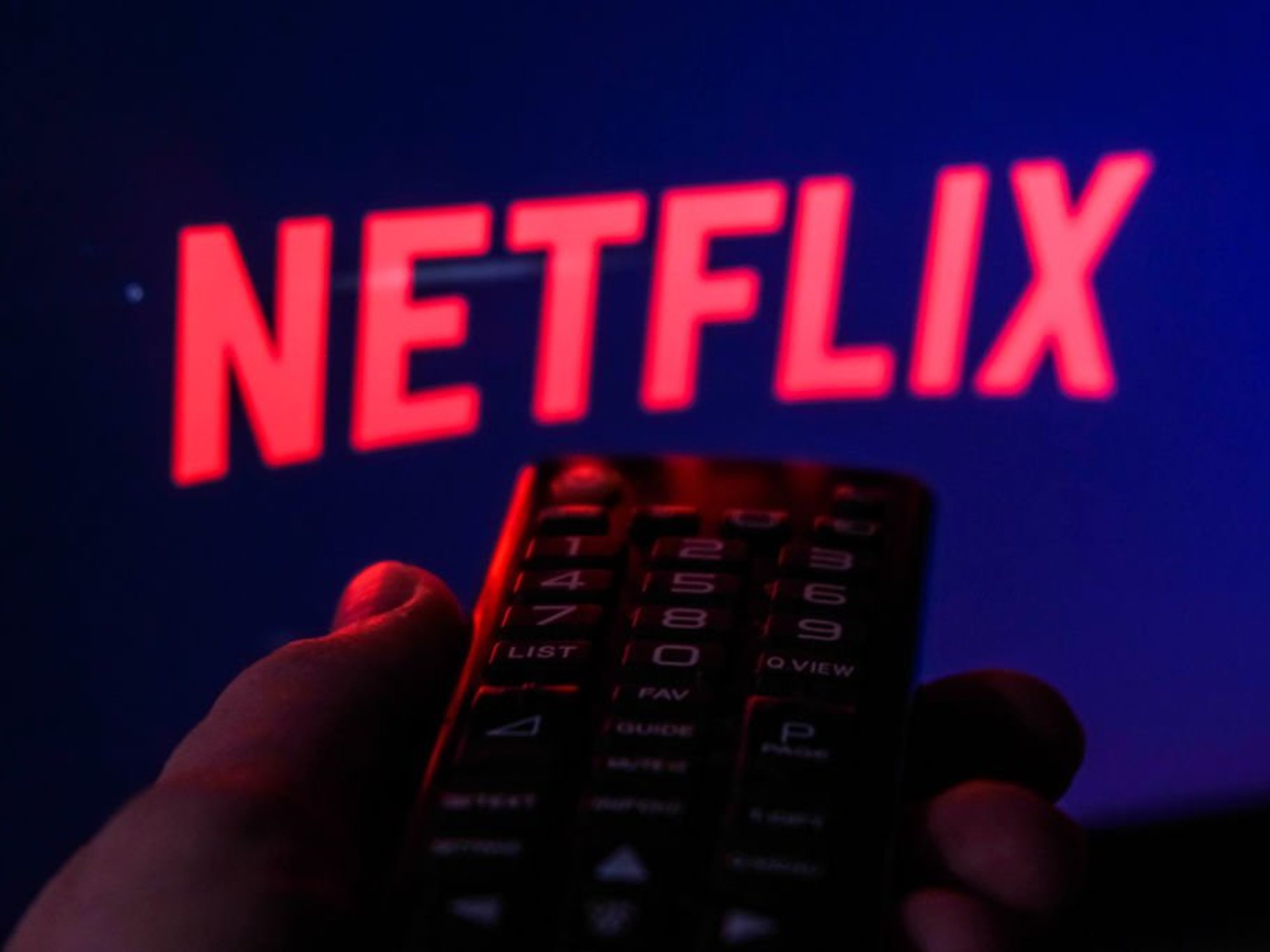 Hand holding TV remote in front of Netflix logo