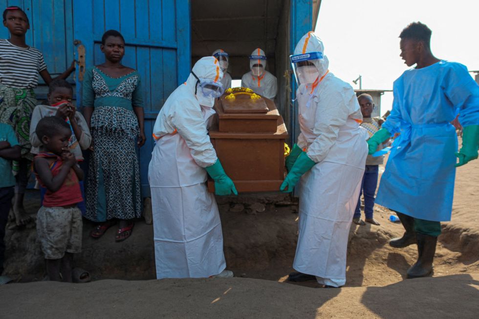 Health workers carrying a coffin out of a building wearing protective clothing