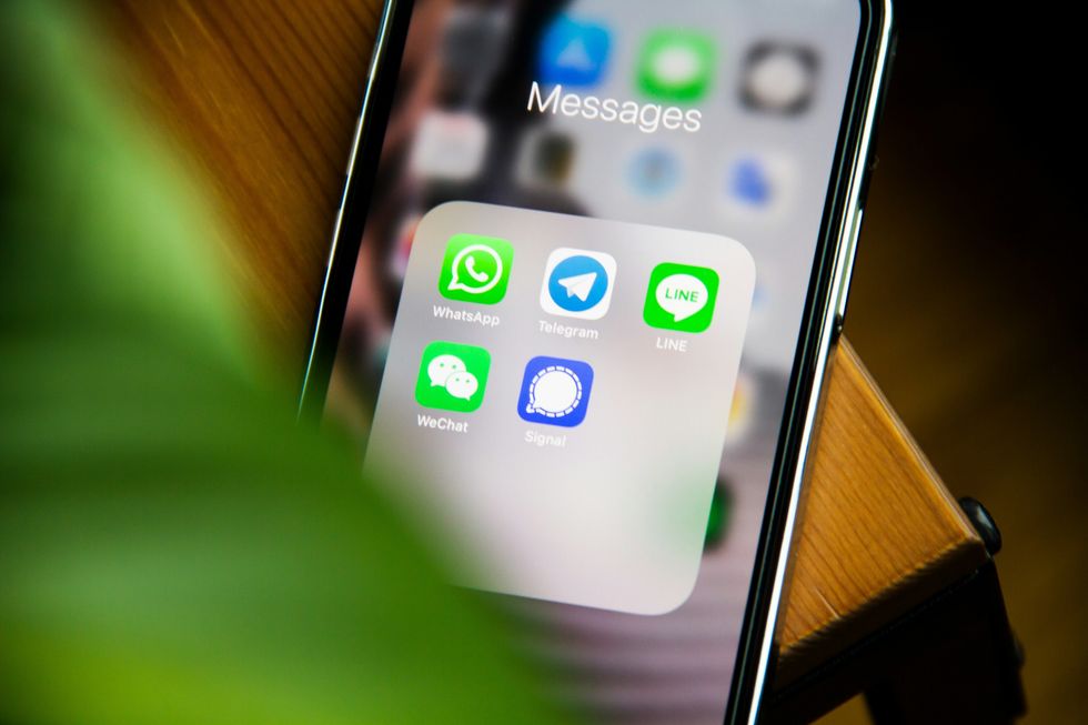 iphone pictured on table with folder of messaging services shown on-screen including whatsap, telegram and signal 