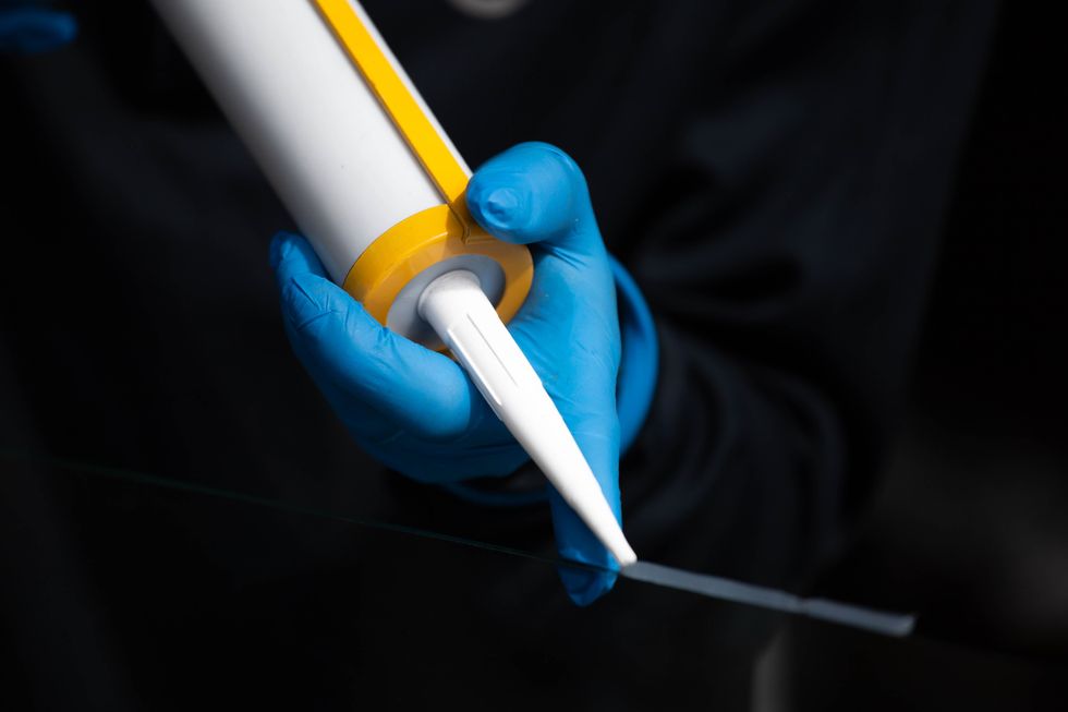 Person applying a white tube of sealant wearing blue gloves