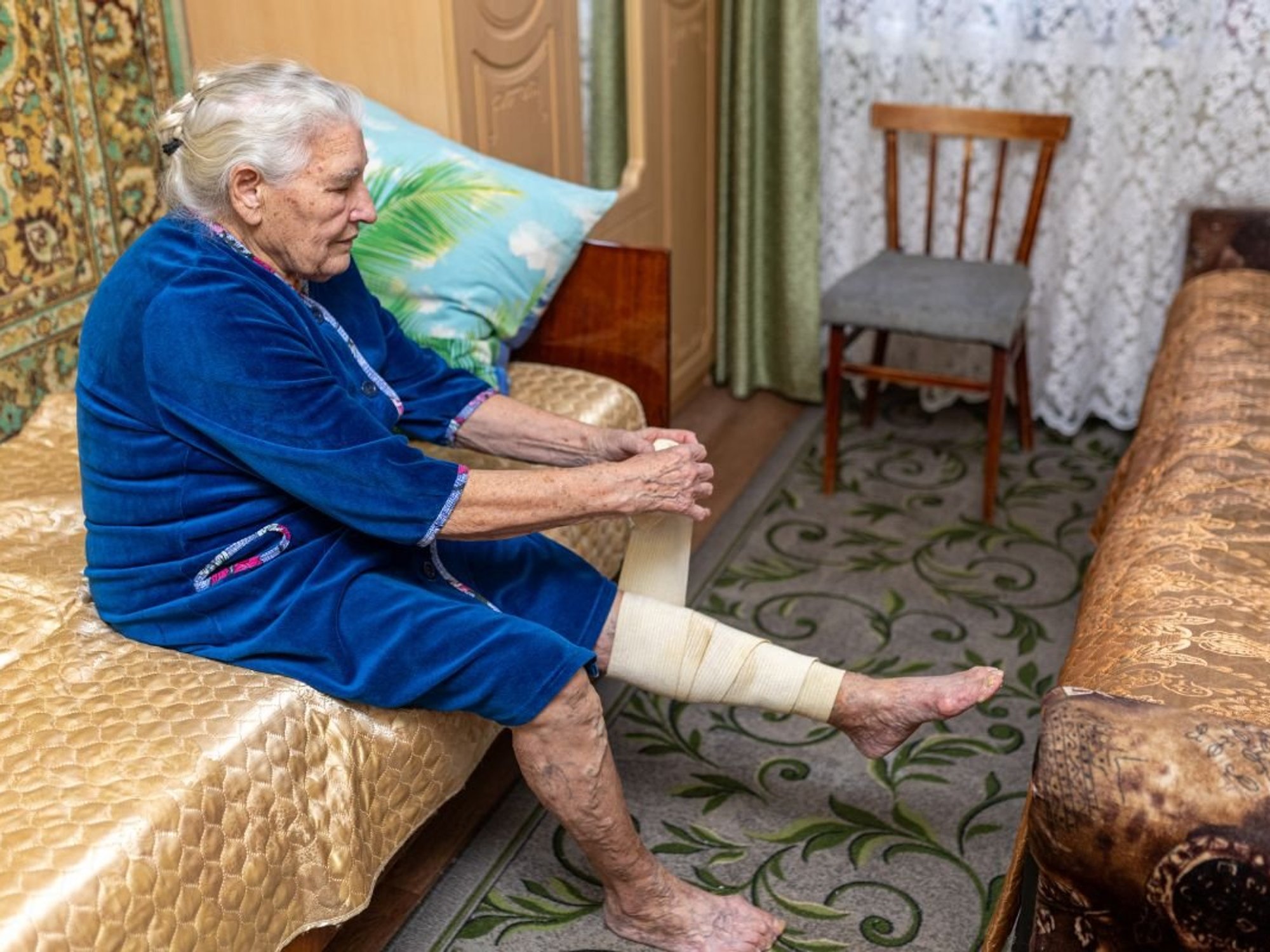 SENIOR WOMAN WRAPPING LEG IN COMPRESSION STRAP