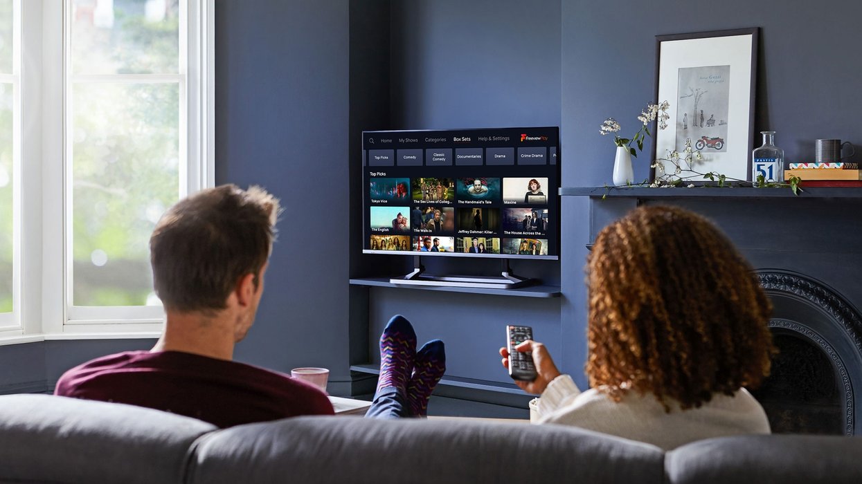 two people sat on the sofa watching freeview with a remote control in their hand