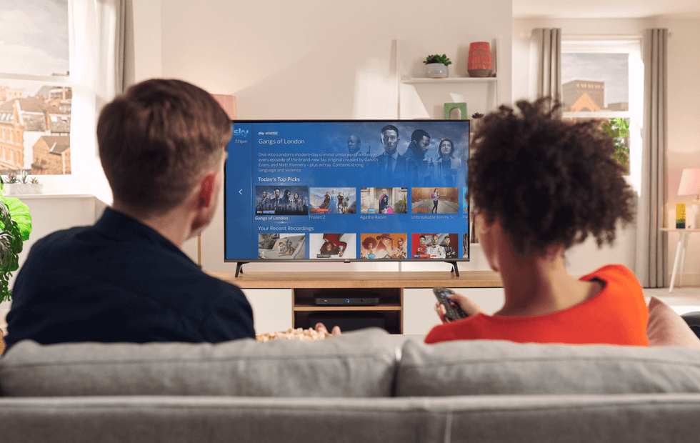 two people sit on a sofa watching sky tv on a flatscreen television