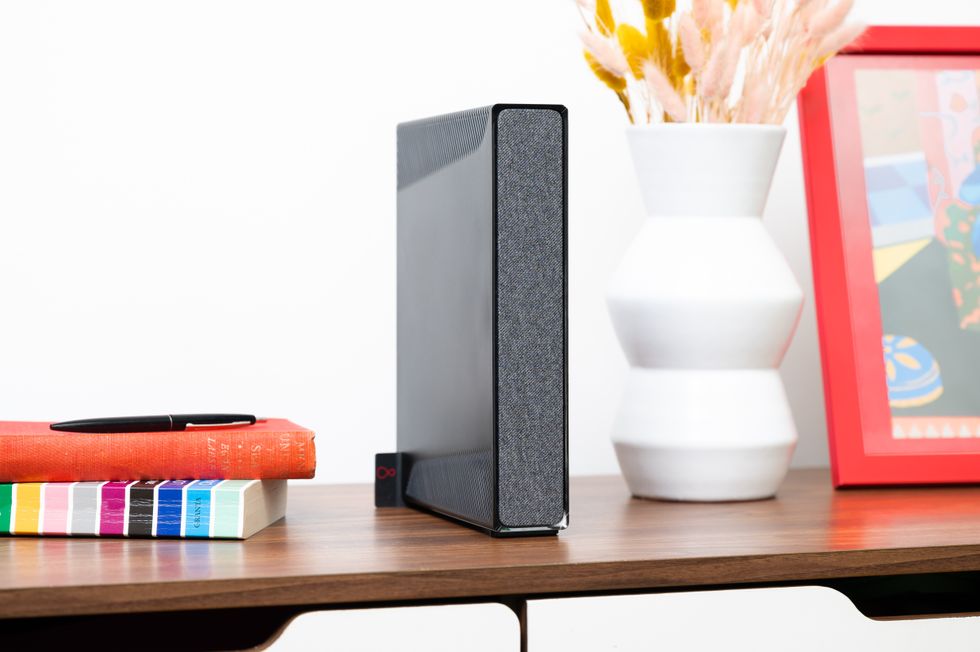 virgin media hub 5 wi-fi router is pictured on a wooden shelf with dried flowers and photo frames nearby