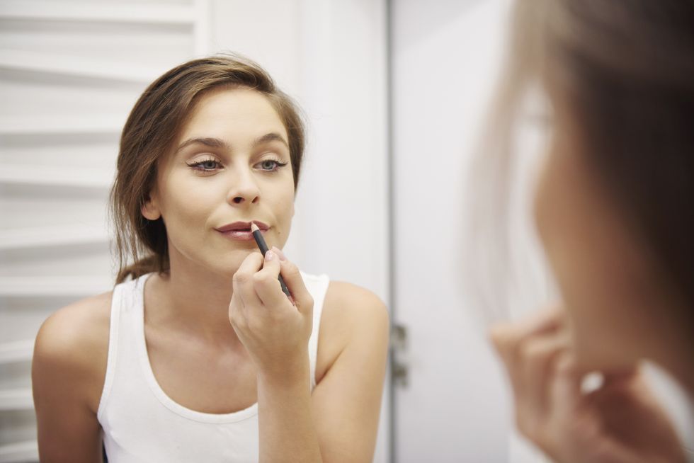 Woman applying a lip liner, looking in the mirror