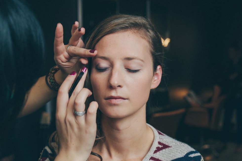 Woman applying makeup onto another brunette woman sitting down