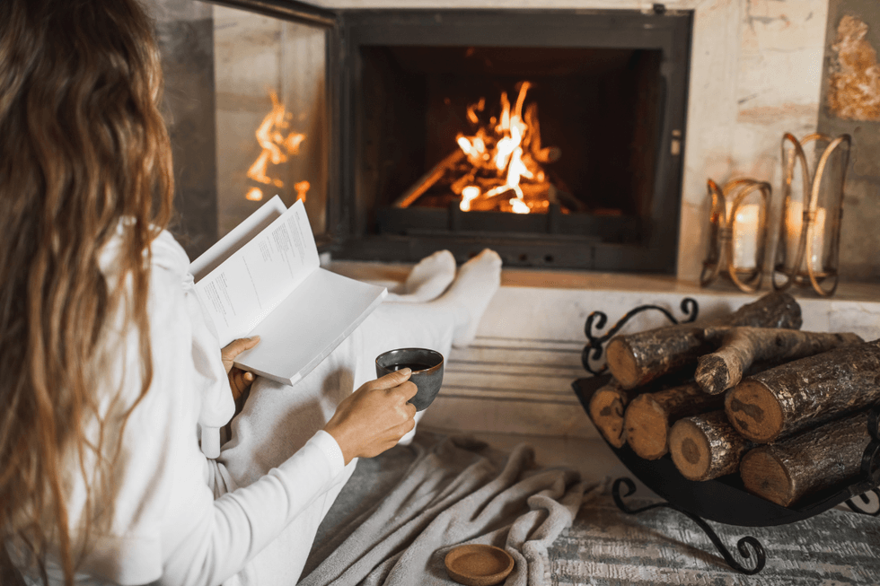 Woman holding a book and cup of tea in front of a fire