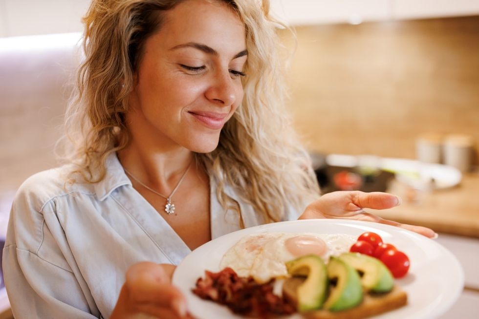 Woman holding plate with eggs, avocado, toast, tomatoes