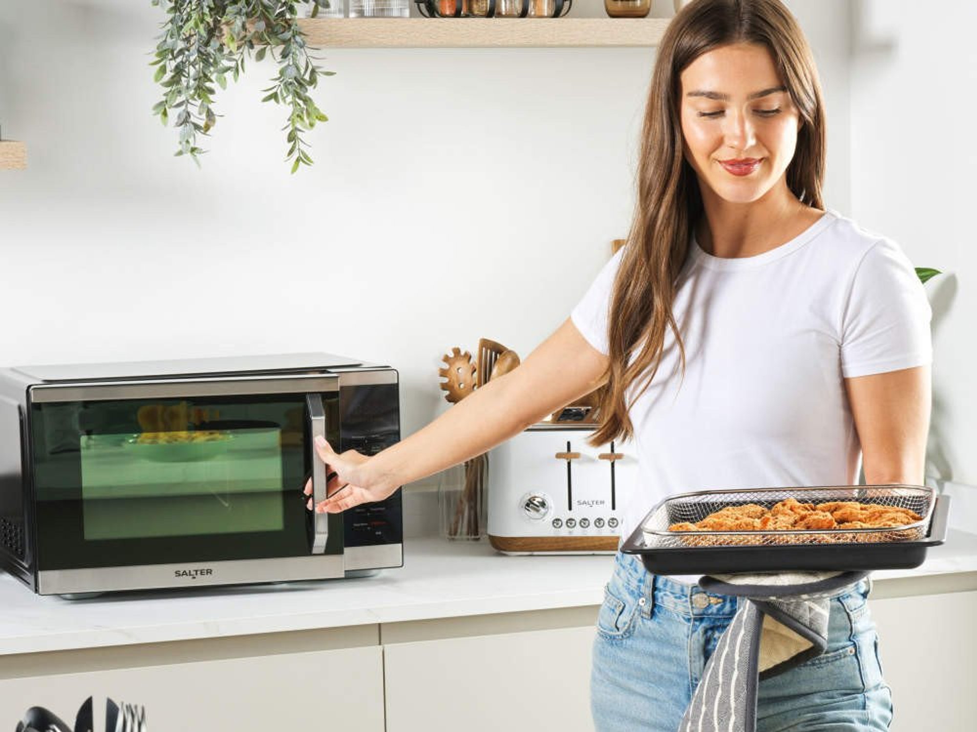 Woman holding tray of food next to Salter DuoWave two-in-one air fryer and microwave