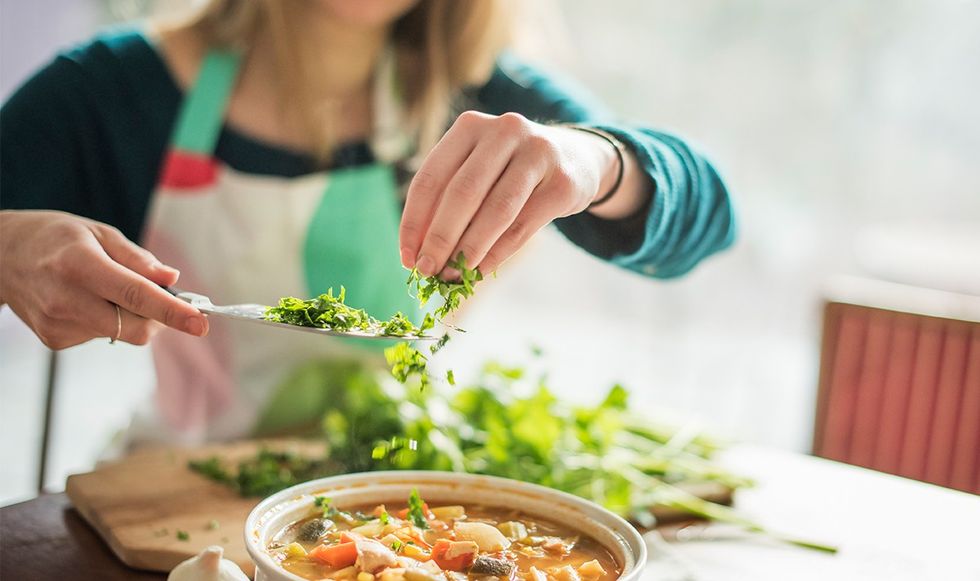 Woman throwing chopped parsley into soup 